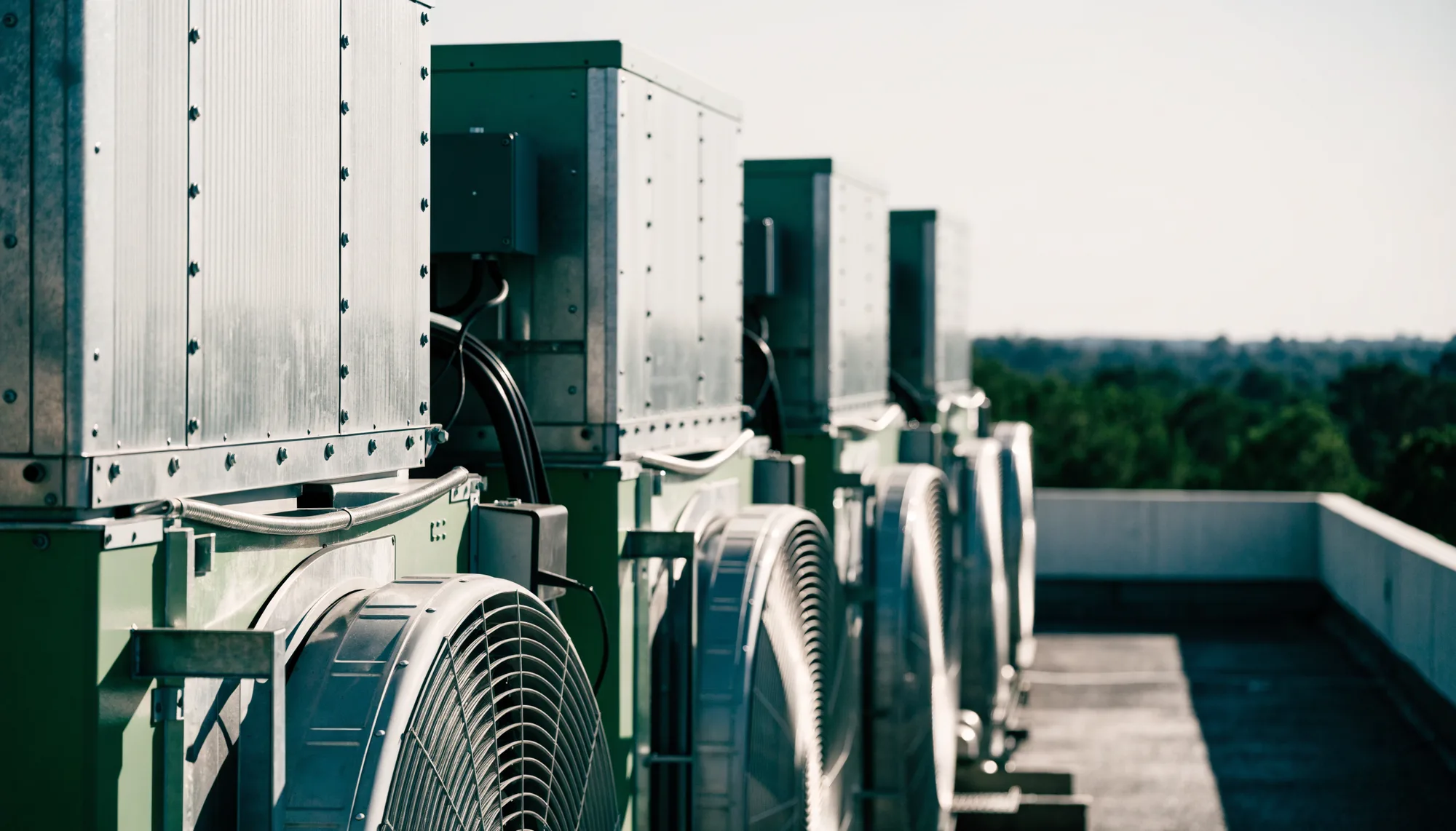 A bank of large air conditioning condenser units and heat pumps in galvanised housings on a flat commercial rooftop.