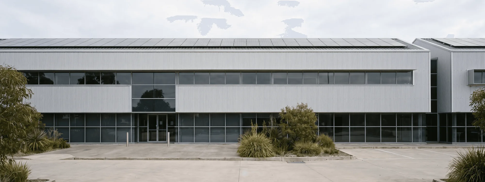 A long two-storey industrial building in profiled steel cladding, with a solar array along the roofline.