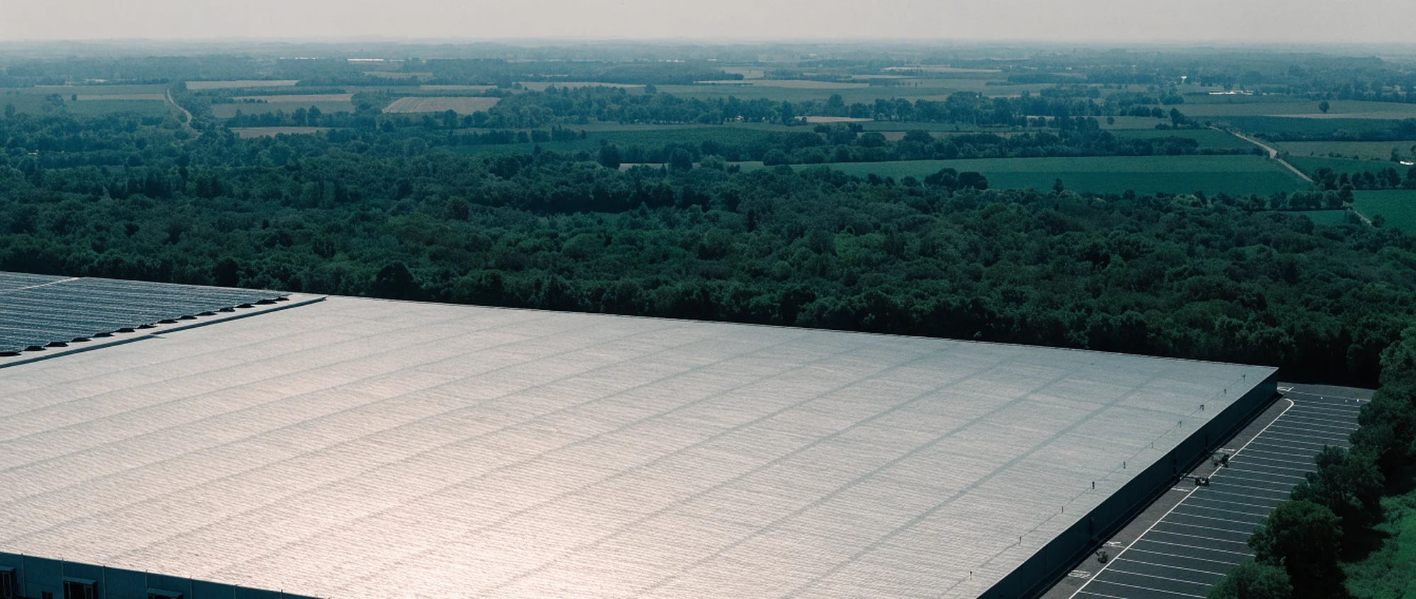 A large warehouse roof seen from the air, with solar panels on one small corner and the rest of the steel deck empty.