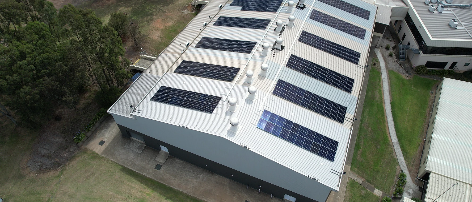 An aerial view of the arrays across the main roof at Valentine Sports Park, with the car park and playing fields beyond.